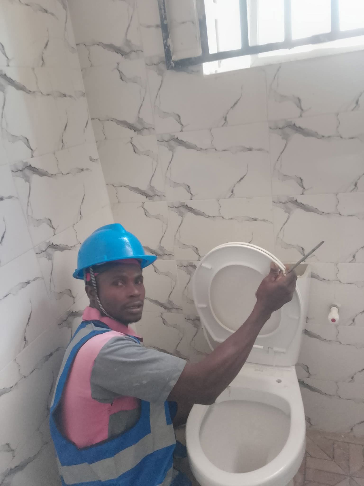 Princekay plumber fitting a WC seat in a marble-tiled bathroom